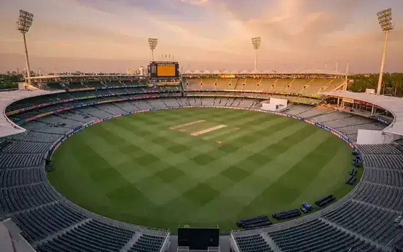 Cricket batsman playing a cover drive at a sunlit stadium